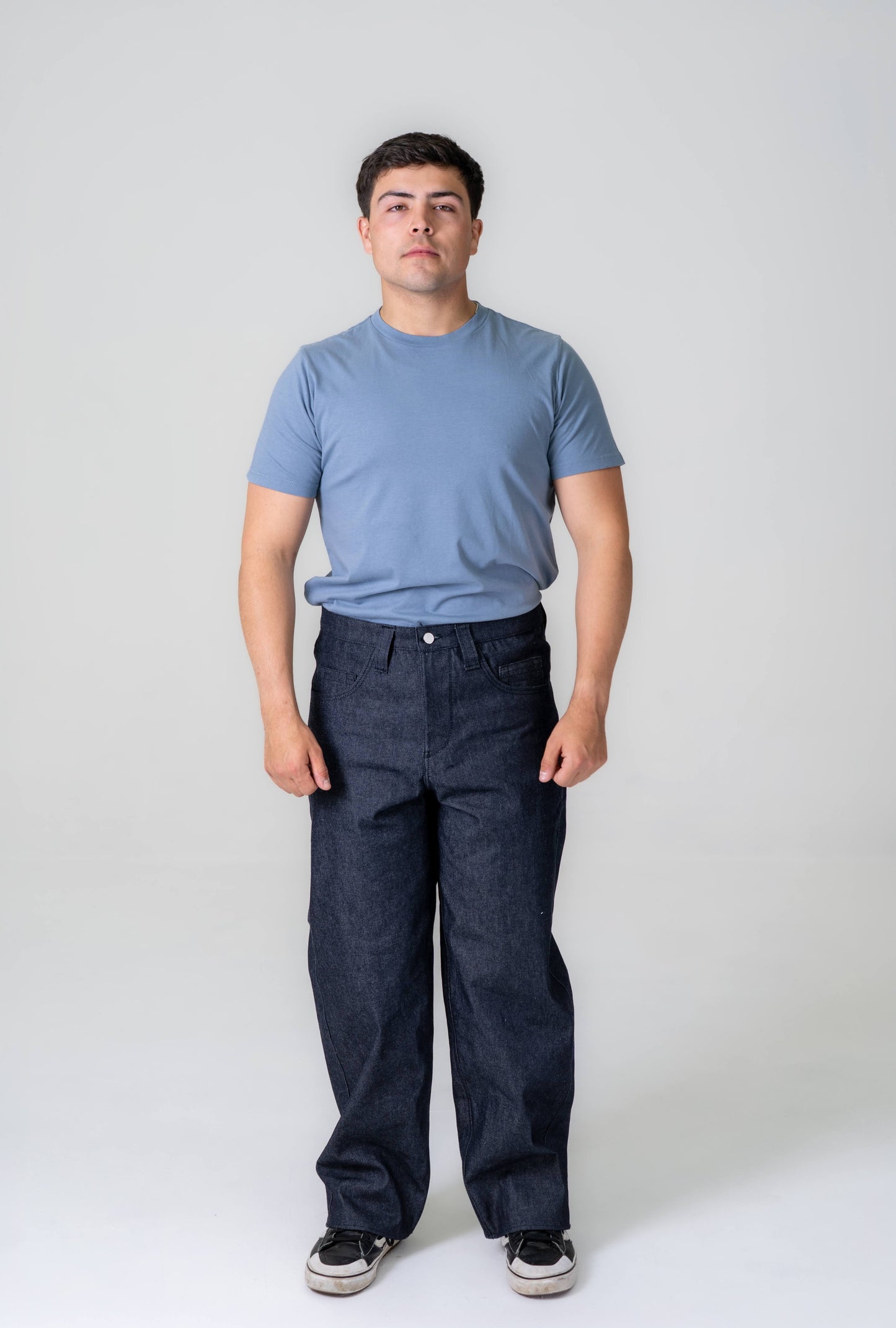 Man wearing a blue t-shirt and dark jeans against a white background