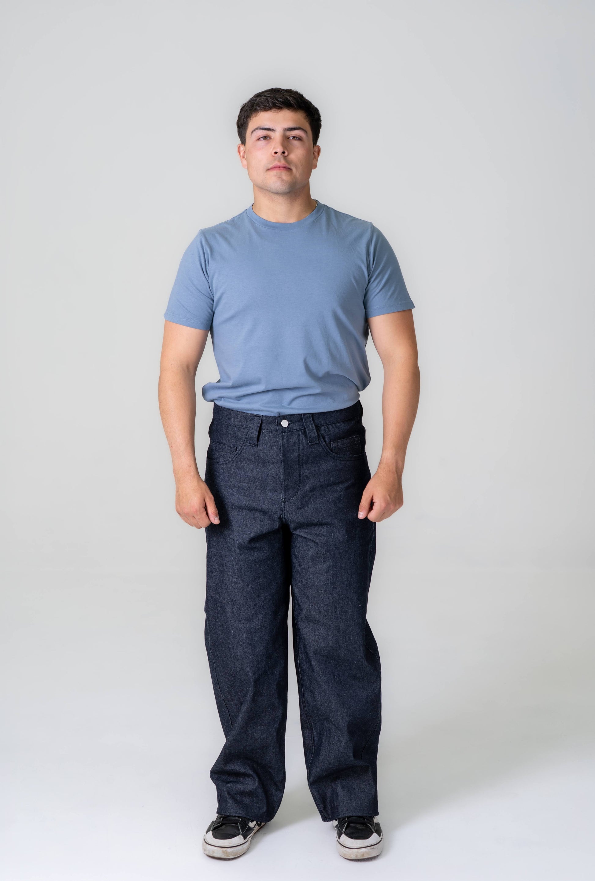 Man wearing a blue t-shirt and dark jeans against a white background