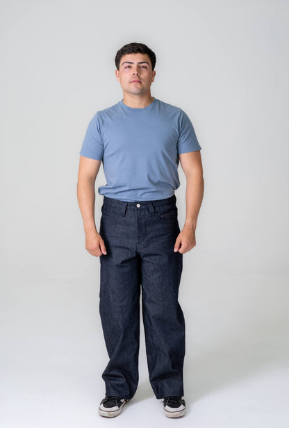 Man wearing a blue t-shirt and dark jeans against a white background