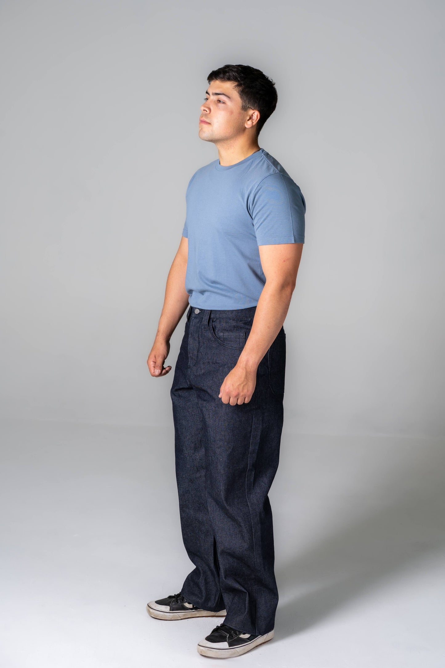 Man wearing a blue t-shirt and dark pants against a gray background