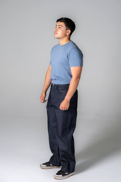 Man wearing a blue t-shirt and dark pants against a gray background