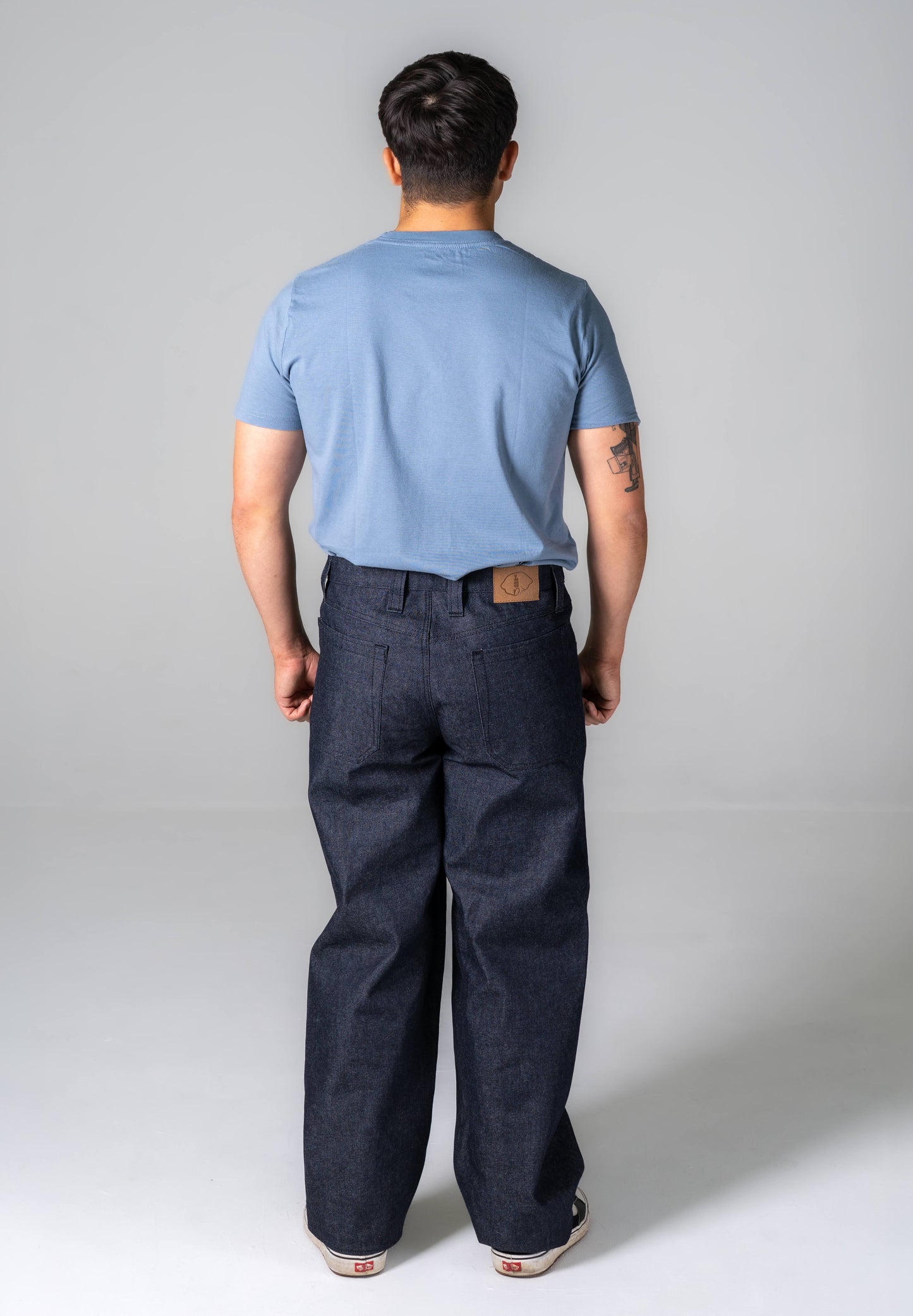 Person wearing a light blue t-shirt and dark pants on a plain background
