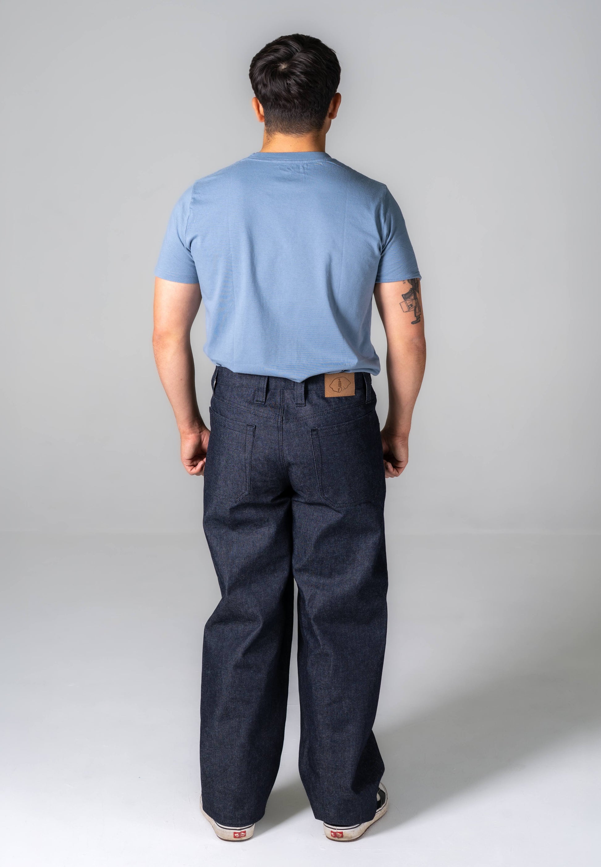 Person wearing a light blue t-shirt and dark pants on a plain background