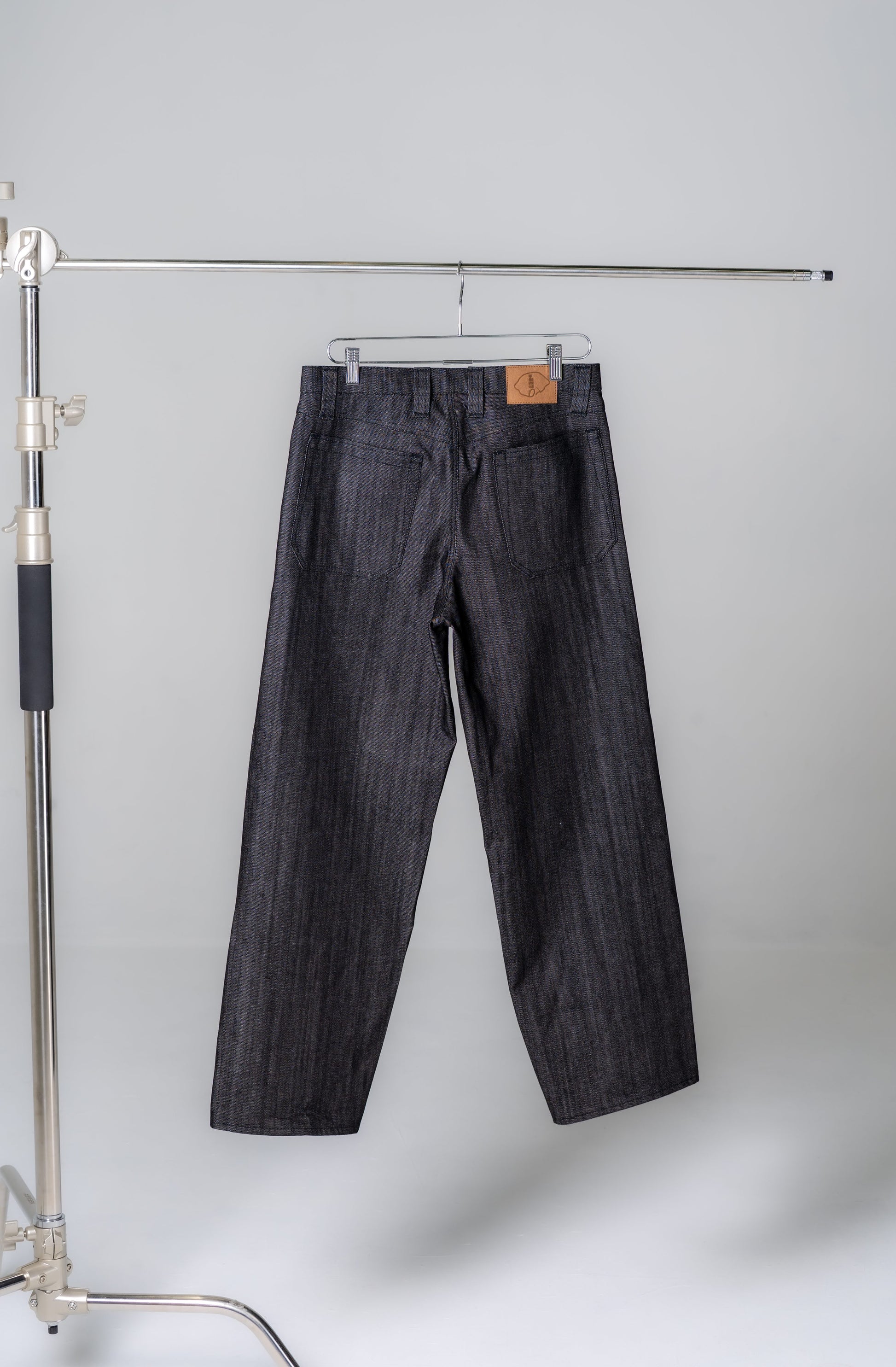 Dark denim jeans hanging on a rack against a plain background