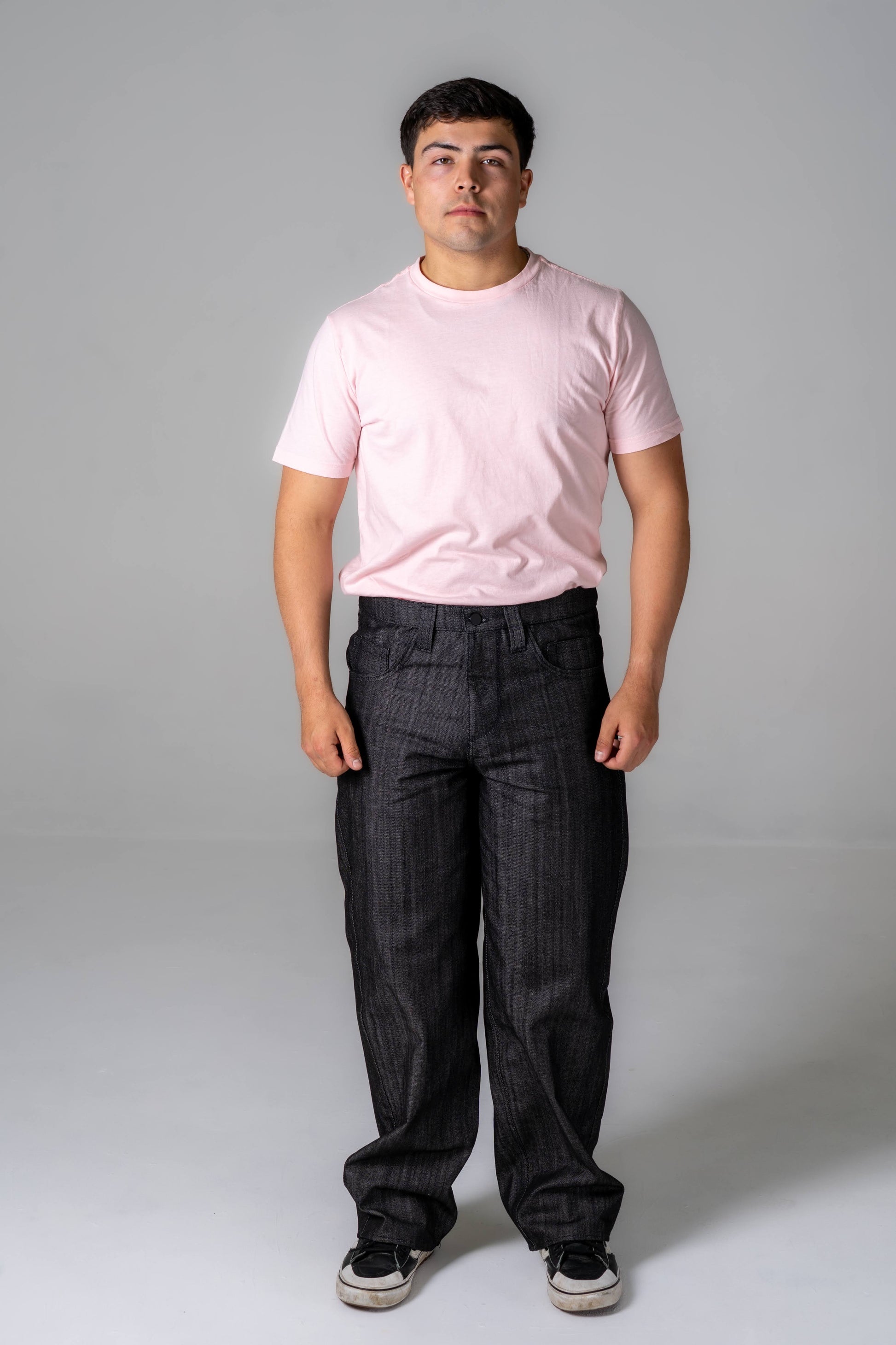 Man wearing a pink t-shirt and dark pants on a gray background