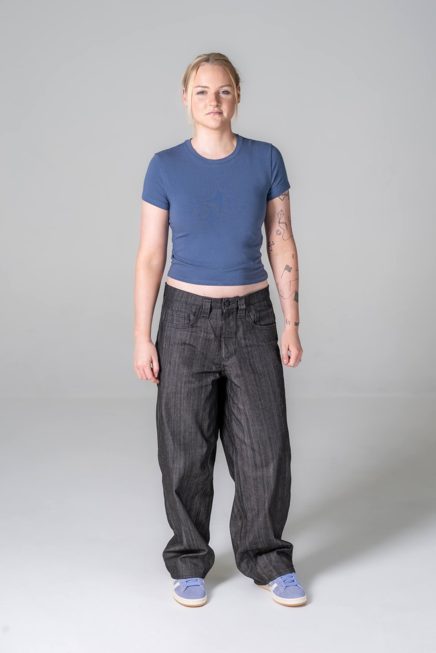 Person wearing a blue crop top and dark pants on a gray background