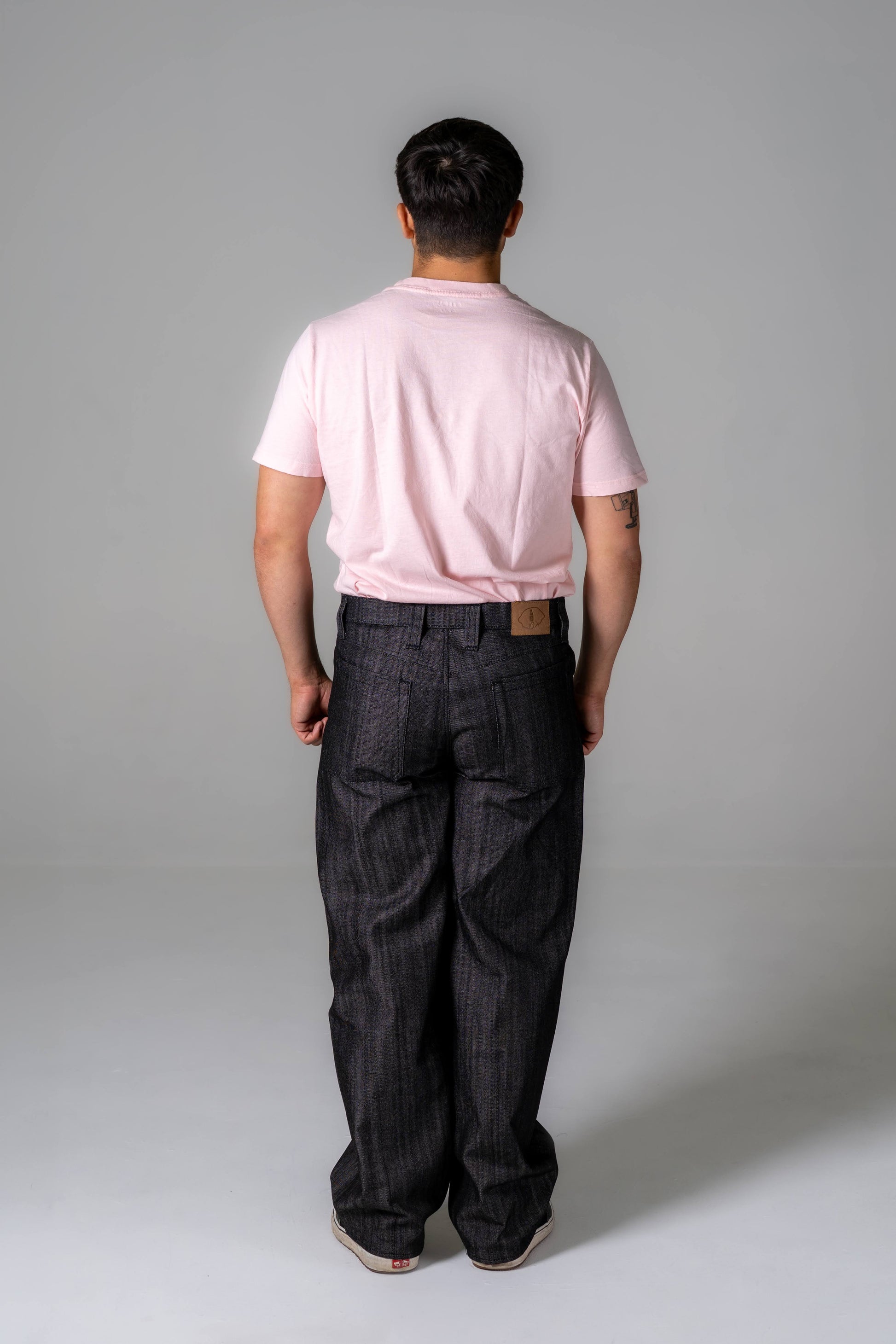 Person wearing a pink polo shirt and dark jeans against a gray background