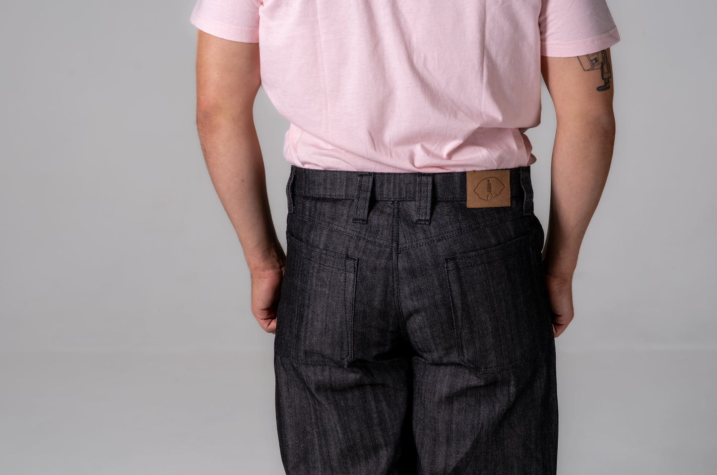 Person wearing a pink shirt and dark plaid pants with a visible brand logo on a gray background