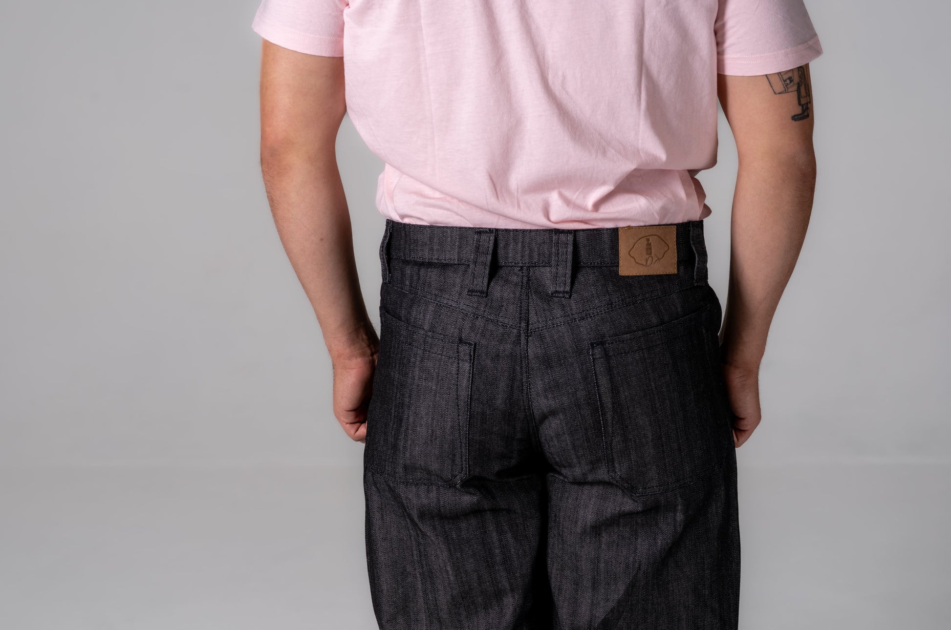 Person wearing a pink shirt and dark plaid pants with a visible brand logo on a gray background