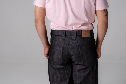 Person wearing a pink shirt and dark plaid pants with a visible brand logo on a gray background