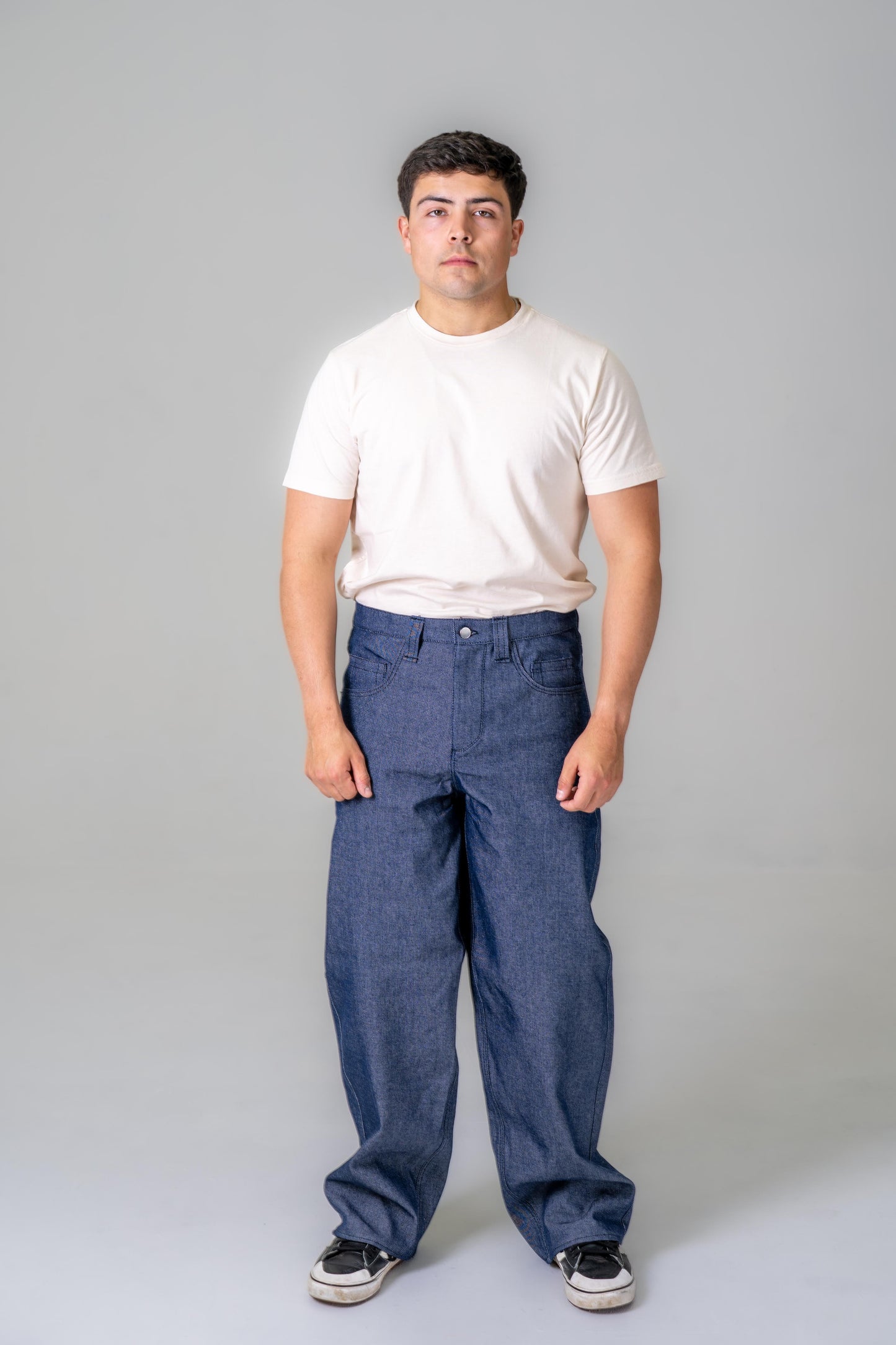 Man wearing a white t-shirt and blue jeans against a gray background