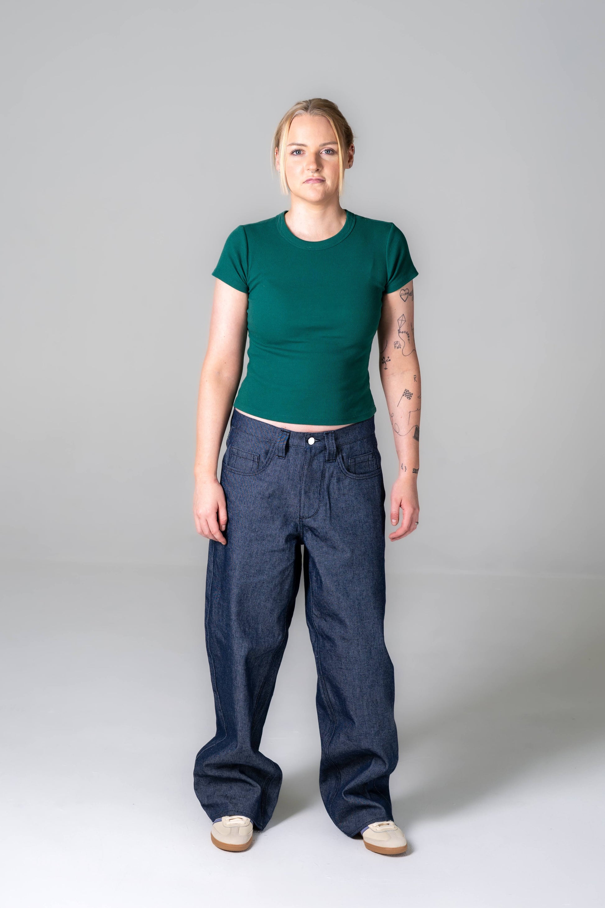 Person wearing a green t-shirt and blue jeans on a gray background
