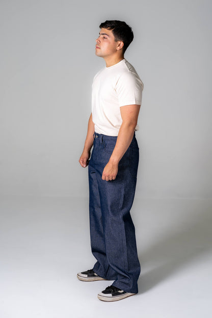 Person wearing a white shirt and blue jeans standing against a plain background